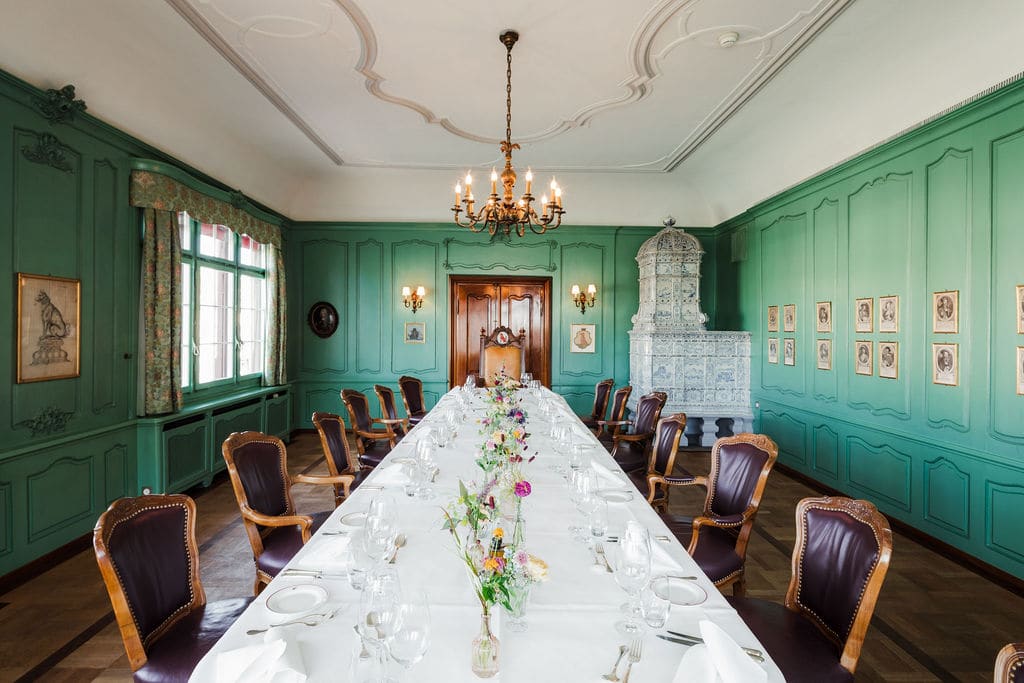 Zimmer mit grüner Täfelung, Porträts an den Wänden und langer Tafel