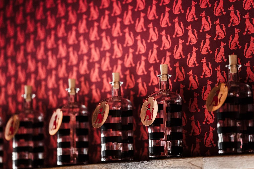 Bar mit einer Reihe von Gin-Flaschen vor rot gemusterter Wand